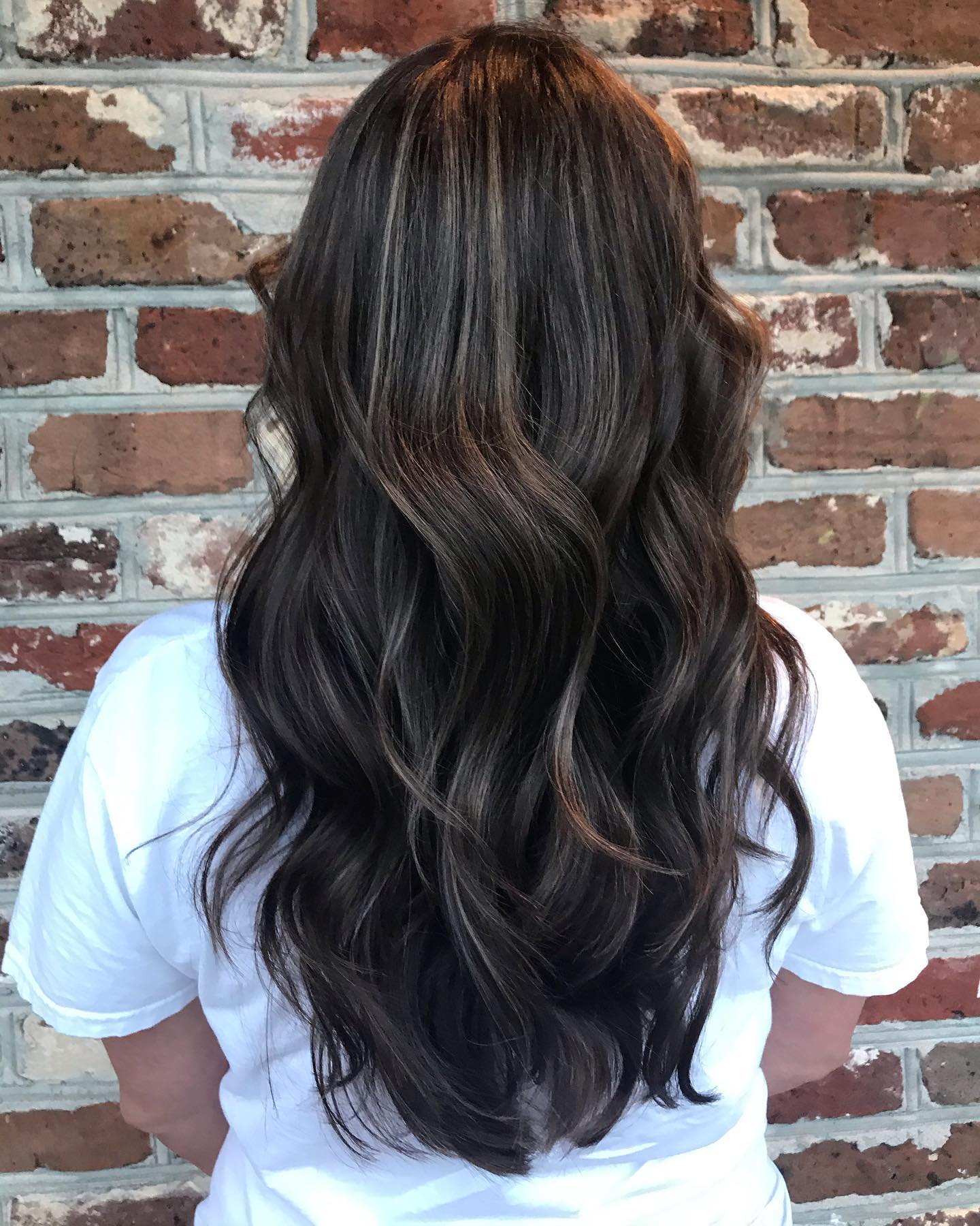 Long dark waves with soft dimension, photographed against the salon’s brick wall
